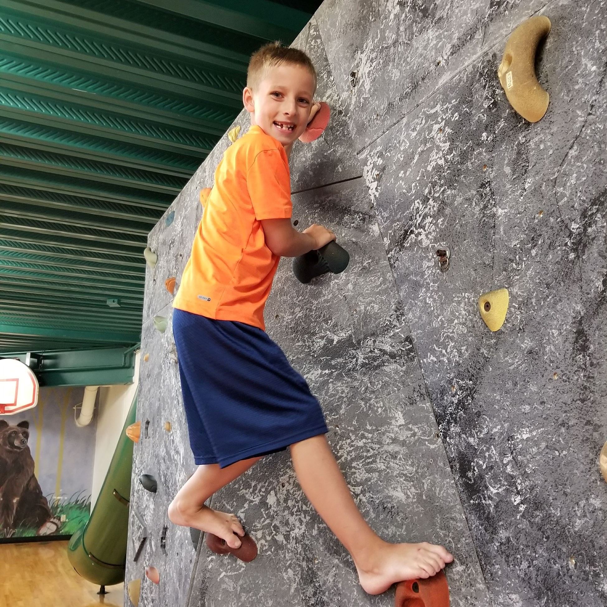 Boy in orange shirt climbing the rock wall in the gym