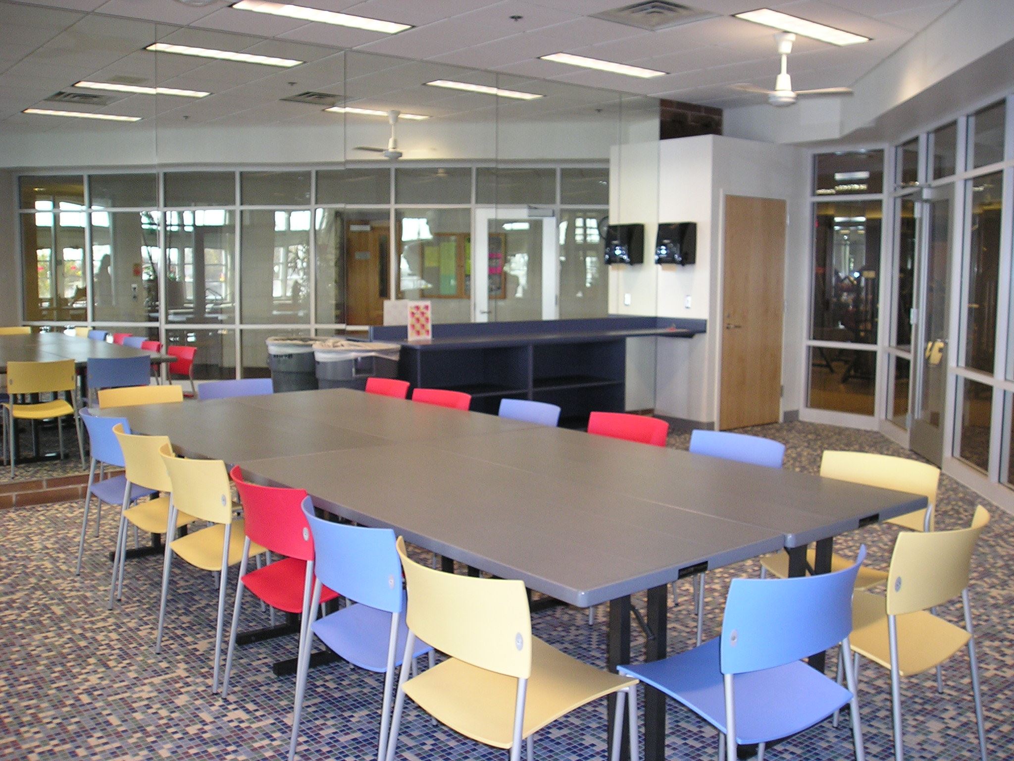 Photo depicts the river birch room with tables set up for 17, windows facing the hallway behind tabl