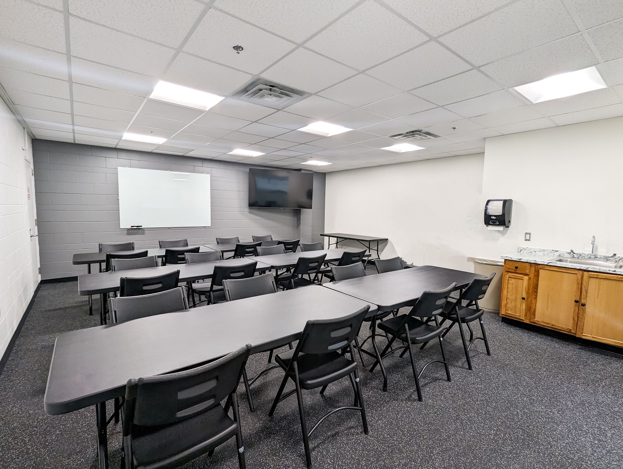 Rink Side room with tables and chairs set up , white board and TV, countertop and sink 